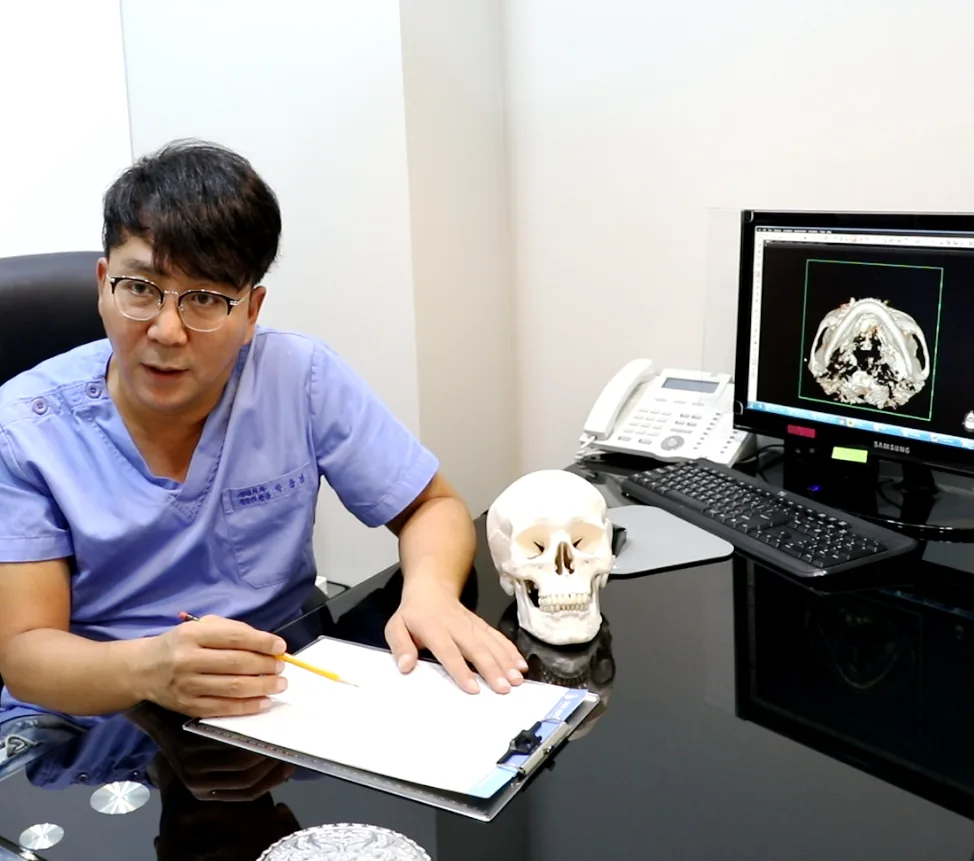 상담 책상에서 두개골 모형과 영상을 옆에 두고 설명하는 박용남 대표원장